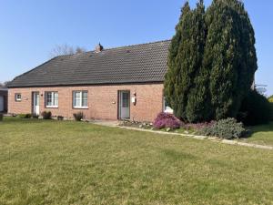 Una casa de ladrillo con un gran árbol delante de ella. en NEU! Ferienhaus Leybucht in Norden, en Norden