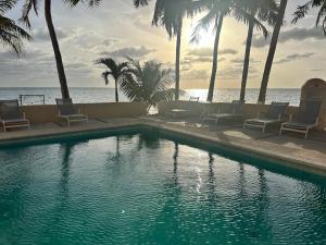 a swimming pool with chairs and palm trees and the ocean at A la Orilla del mar Puerto Juarez Cancun in Cancún