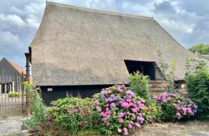 an old house with a thatched roof and flowers at Schaapskooi 20 in Dwingeloo