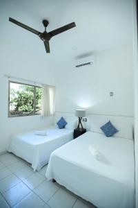 two beds in a white room with a ceiling fan at Kinta Kan Cabañas Hotel Playa del Carmen in Playa del Carmen