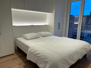 un lit blanc dans une chambre avec une grande fenêtre dans l'établissement Westende Zeezicht, à Middelkerke