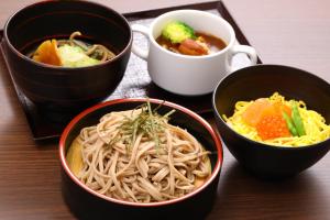a table with bowls of noodles and a cup of soup at Dormy Inn Matsumoto in Matsumoto