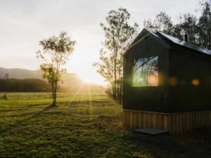 a small black shed in a field with the sun in the background at Secluded Off-Grid Cabin in the Hunter Valley - Leo in Pokolbin +4 photos