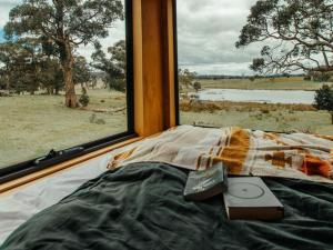 a bed with a remote control on it next to a window at Cosy Off-Grid Cabin with Lake View - Galeb in Pipers Creek