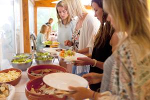 un grupo de mujeres de pie alrededor de una mesa comiendo comida en Amar Hostel & Suites, en Ericeira