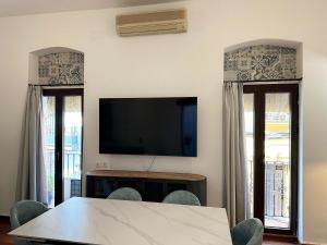 ein Esszimmer mit einem Tisch und einem Fernseher und zwei Fenstern in der Unterkunft La Alcazaba de Triana in Sevilla + 23 Fotos