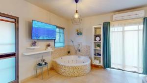 um banheiro com banheira e uma tv na parede em סוויטות טיפאני של רשת לב הגולן - וילה וסוויטות עם בריכות מחוממות פרטיות מחוממות ומקורות em Had Nes