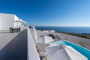 een zwembad met witte parasols en de oceaan bij La Maltese Residence in Imerovígli