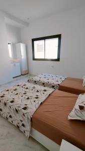 two beds in a white room with a window at Résidence Yasmine in Ksour Essaf