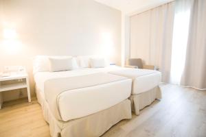 a white bedroom with two beds and a desk at Hotel Albufera in Alfafar
