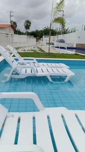 a group of white lounge chairs in a swimming pool at Casa Condomínio Reserva do Delta in Parnaíba