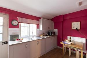 a kitchen with purple walls and a table and a clock at Bishop Lightfoot Cottage in Bishop Auckland +21 photos