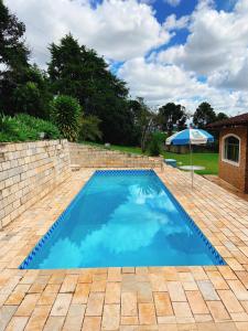 a blue swimming pool with an umbrella in a yard at Sítio Pand'Oro in Atibaia