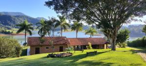a house on a hill with a tree and a lake at Chalé Represa Suite Varanda Do Sol in Joanópolis
