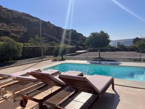 a swimming pool with chaise lounges and chairs next to a mountain at Kythnian Retreat in Kithnos