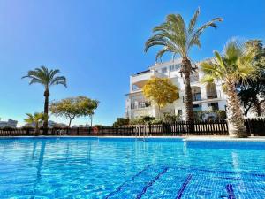 a swimming pool in front of a building with palm trees at Stunning frontline apartment with golf views and pool in Sucina