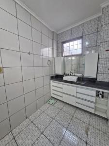 a white tiled bathroom with a sink and a mirror at Loft de Quarto e Sala em Vila in Belém
