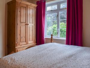 a bedroom with a bed and a window with pink curtains at Valentine Cottage in Keswick +8 photos