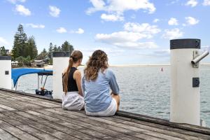 two women sitting on a dock looking at the water at Pumicestone Passage Waterfront Escape in Caloundra