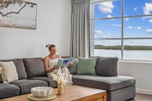 a woman sitting on a couch reading a book at Pumicestone Passage Waterfront Escape in Caloundra
