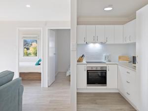 Marg's - Oceanstays - Oceanfront في Brooms Head: مطبخ مع دواليب بيضاء وغرفة معيشة مع سرير