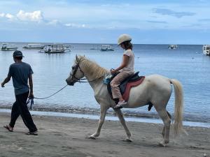 a girl riding a horse on the beach with a man at Reef Seen Divers' Resort in Pemuteran