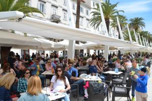una multitud de personas sentadas en mesas bajo sombrillas en Apartments & Rooms Dujam, en Split
