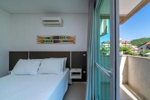 1 Schlafzimmer mit einem Bett und einem Balkon mit einem Fenster in der Unterkunft Apartamento a 150 metros da Praia Bombinhas com 110m2 Natureza e Praia juntos Apt Completo pra toda família com Elevador #Uma verdadeira Experiência# in Bombinhas