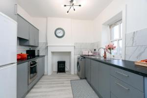 una cocina con armarios grises y un reloj en la pared en Nelson cottage- WiFi-parking-M65-Hospital- town -food- shops- contractor, en Nelson 88 fotos más