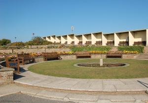 a park with benches and a fountain in front of a building at 2 Museum Cottages in Sheringham