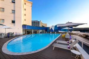 a swimming pool with chairs and umbrellas next to a building at Hotel Sky Sandton in Johannesburg