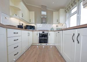 a white kitchen with white cabinets and a wooden floor at Athelington Hall Farm Lodges in Horham +81 photos