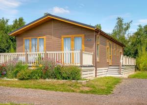 a small wooden house with a porch and flowers at Otters Mead Boutique Lodges in Beetley