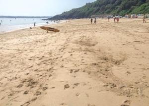 a group of people walking on a beach with a surfboard at Stream Valley Holiday Park in Penzance
