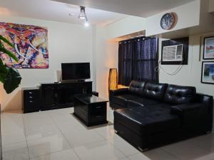 a living room with a black leather couch and a television at Lourdes Bedsit Horizon 101 in Cebu City