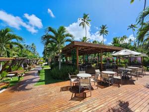 une terrasse en bois avec des tables, des chaises et des palmiers dans l'établissement Amura Carneiros - Pé na areia - Trecho Exclusivo, à Praia dos Carneiros