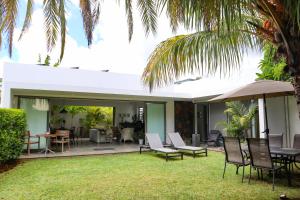 an outdoor patio with chairs and tables and an umbrella at Villa koki Bonheur in Grand-Baie