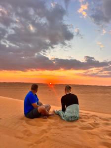 two men sitting on the beach watching the sunset at Tranquility Camp in Al Raka