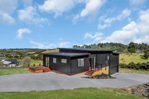 a black house with a black roof on a field at Central Couples Retreat - Mangawhai Heads Unit in Mangawhai
