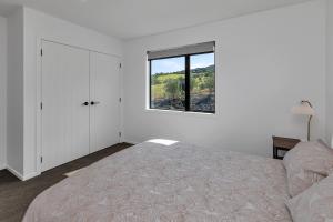 a white bedroom with a bed and a window at Central Couples Retreat - Mangawhai Heads Unit in Mangawhai