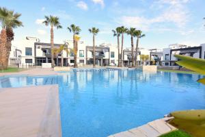 a large swimming pool with palm trees and buildings at Magnifico apartamento en Oasis Beach in Playa Flamenca