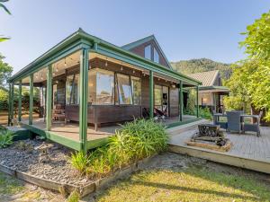 a green home with a wooden deck and a porch at Beaumont Beach Retreat - Pauanui Holiday Home in Pauanui