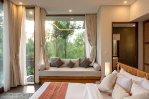 a bedroom with a bed and a window with a couch at Villa Suarga Des Anicca in Ubud