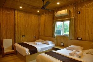 two beds in a room with wooden walls and a window at Tarapith Tapabon Eco Resort in Tarapith