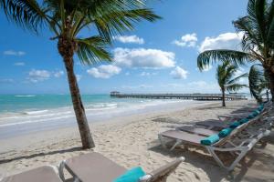 a row of chaise lounges on a beach with a pier at Impressive Punta Cana - All Inclusive in Punta Cana