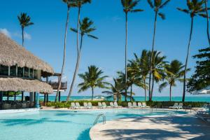 a resort swimming pool with palm trees and the ocean at Impressive Punta Cana - All Inclusive in Punta Cana