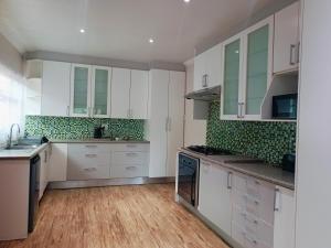 a large kitchen with white cabinets and green tiles at 21 On Coetzee Guest House in Bloemfontein