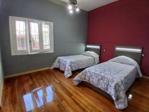 2 camas en una habitación con paredes rojas y suelo de madera en Hospedaje DUDOMU, en Buenos Aires
