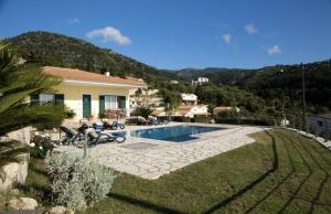 a couple sitting in chairs next to a house with a swimming pool at Pantheon Villas in Agios Nikitas
