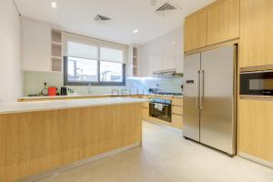 Una cocina con gabinetes de madera y un refrigerador de acero inoxidable. en Pool and Sea Views 4BR and Assistant's Room Villa with Own Pool, Sharm - Al Dana Villa, Al Dana Island by Deluxe Holiday Homes, en Fujairah